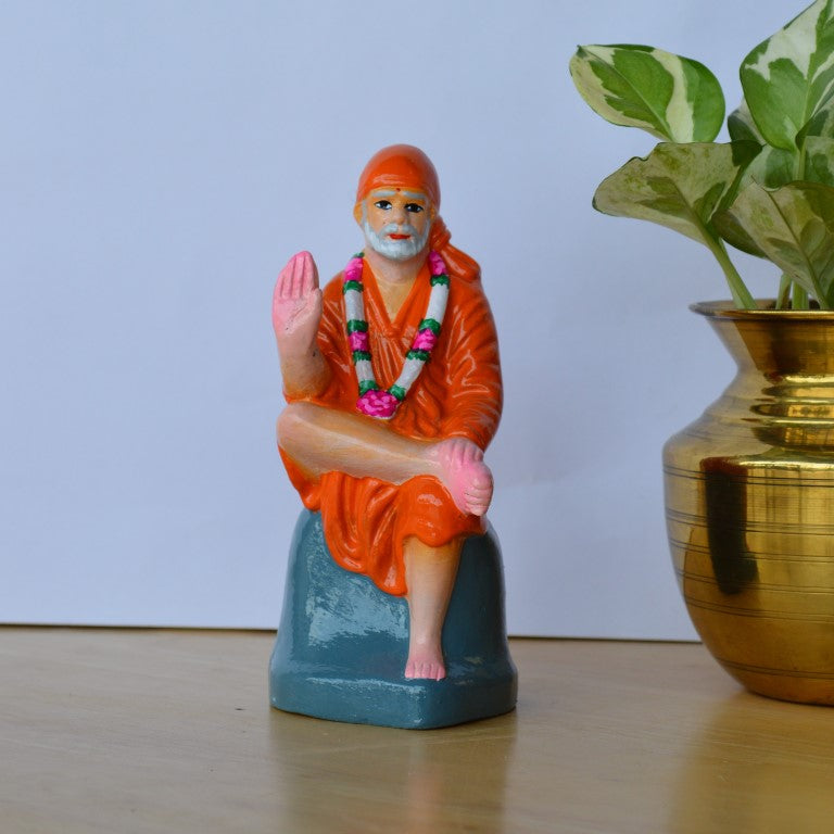 Handcrafted medium-sized Sai Baba idol in an orange robe seated on a rock, adorned with a garland, perfect for Navarathri Golu or home decor.