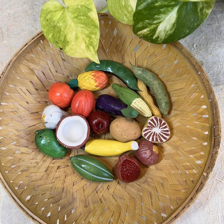 A basket of miniature fruits and vegetables for Navarathri Golu, including items like coconut, banana, brinjal, corn, and more.