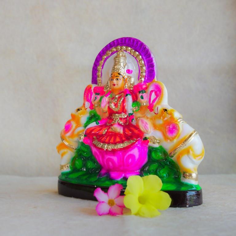 Hand-painted Navarathri Golu doll of Gajalakshmi seated on a lotus with elephants, adorned with vibrant colors and intricate details.