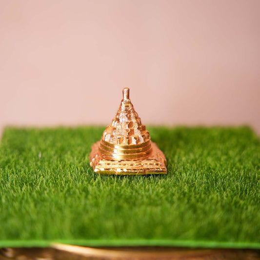 Golden brass Meru Shree Yantra displayed on a green base, showcasing intricate sacred geometry and craftsmanship.