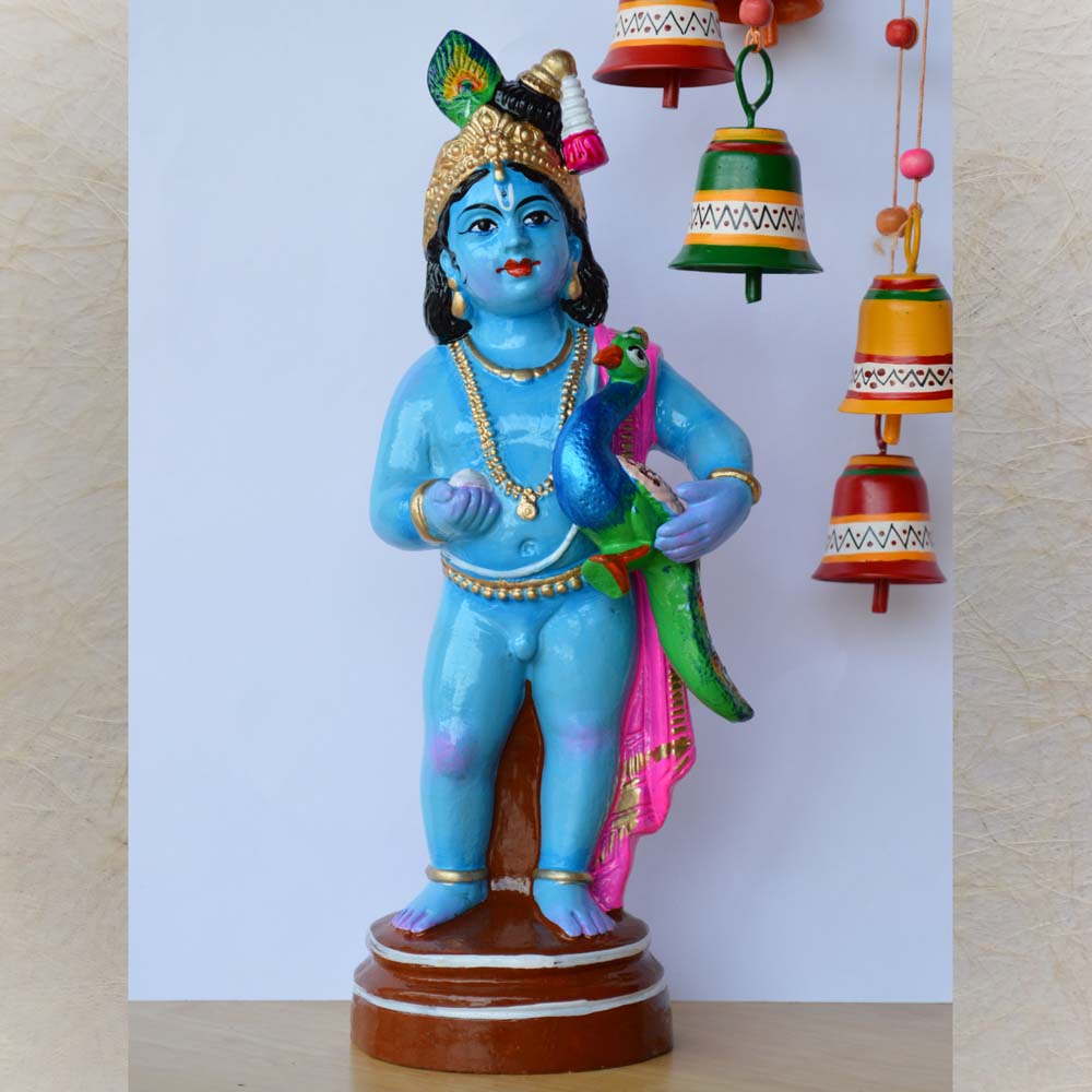 Handcrafted Golu doll of Lord Krishna holding a vibrant peacock, adorned with intricate details and painted in vibrant blue, green, and gold tones.