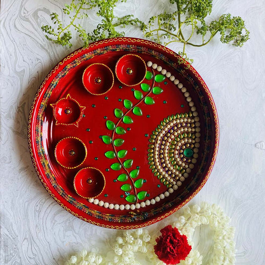 Handcrafted Lustre Red Pooja Thali with 5 cups, decorated with green embellishments, pearls, and artistic patterns, placed on a white textured background with flowers.