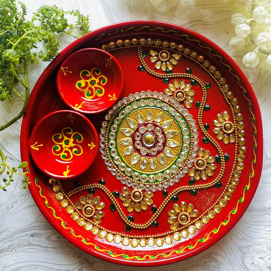 Handcrafted red Pooja Thali with 2 cups, decorated with intricate mandala designs, stones, and floral accents, displayed on a white textured background with greenery.