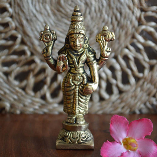 Eternal Balaji brass idol of Lord Venkateswara in a standing posture, with detailed carvings, placed on a wooden surface and decorated with a pink flower.