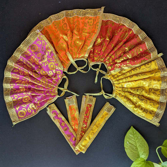 Traditional Devi skirts in vibrant brocade fabric with gold motifs and borders, displayed in red, orange, pink, and yellow on a black background with green leaves.