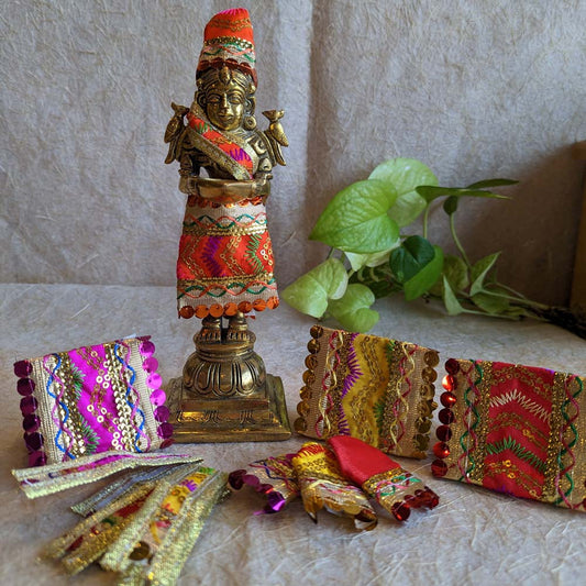 Traditional Sai Vastra set in vibrant colors with zari and sequin detailing, displayed with a brass Sai Baba idol on a textured background.