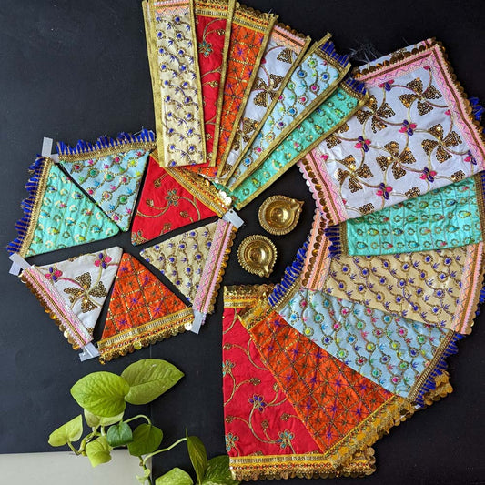 Handcrafted Sai Vastra set in vibrant colors with intricate embroidery, sequins, and zari borders, displayed with decorative brass diyas on a black background.