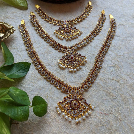 Gold-plated long necklace set with pearl accents and multi-colored stones, showcasing intricate craftsmanship on a textured surface with green leaves.