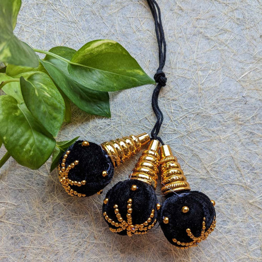 Traditional kunjalam hair accessory with black velvet tassels, gold bead embellishments, and golden cone accents.