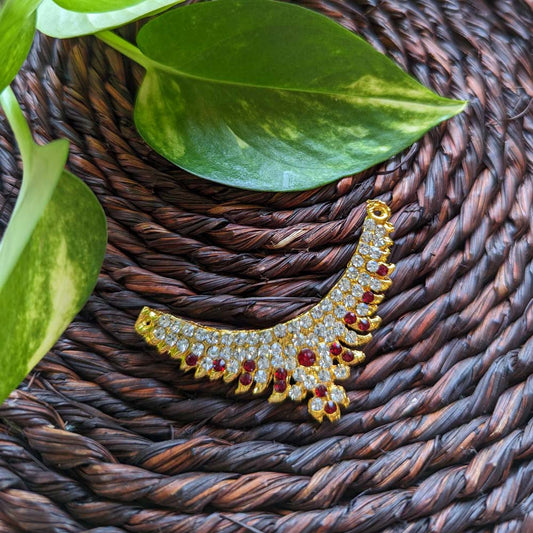 Traditional sticker necklace with ruby and crystal accents on a gold-toned base, displayed on a woven mat with green leaves.