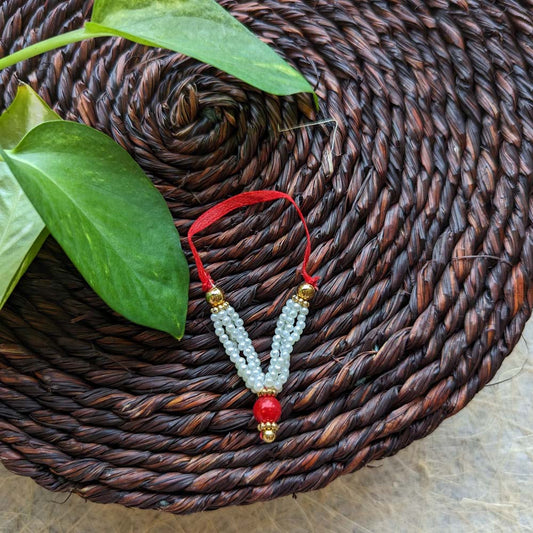 Small traditional garland with pearl-like beads, a red central bead, and gold accents placed on a woven mat with green leaves.