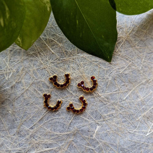 Set of golden nose rings with ruby stone embellishments, displayed on a textured surface with green leaves in the background.