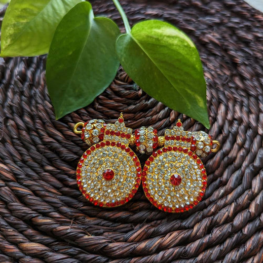 Gold-plated Big Thali Ornament with red and white stones placed on a woven mat with green leaves in the background.