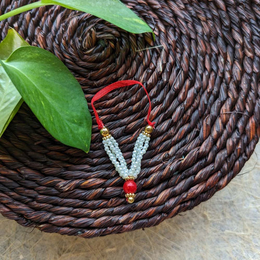 Handcrafted big garland with pearl beads, a red bead centerpiece, and golden accents on a red thread, displayed on a woven mat with green leaves.