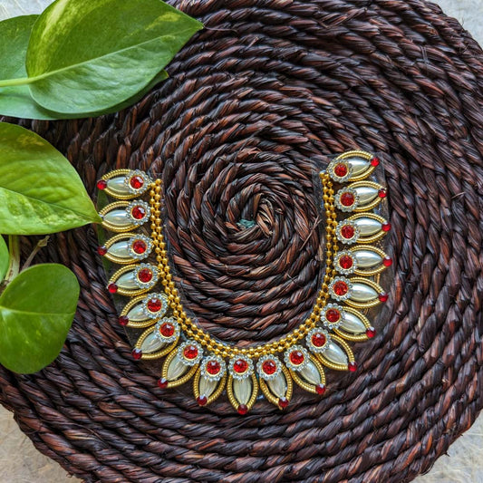 Traditional sticker necklace with gold coin motifs and red-green embellishments, displayed on a woven surface with green leaves.