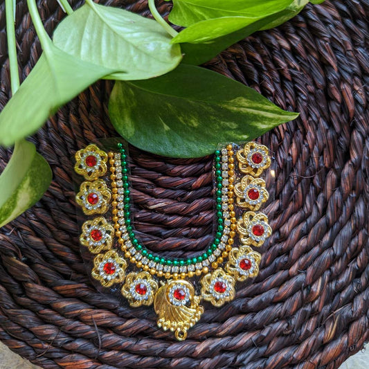 Traditional sticker necklace with gold coin motifs and red-green embellishments, displayed on a woven surface with green leaves.