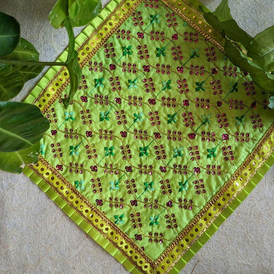 A 13x13 green embroidered Aasan with floral patterns, sequin detailing, and a golden decorative border, displayed with green leaves.