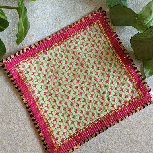 A 22x22 embroidered Aasan with a vibrant green base, pink threadwork, and a decorative sequin border, displayed on a textured surface.