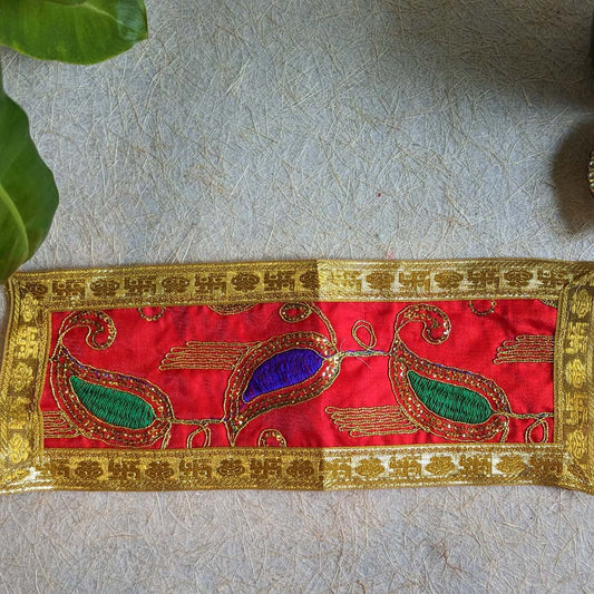 A 12x4 red embroidered Aasan with vibrant paisley patterns, golden detailing, and a rich golden brocade border, displayed on a textured surface.