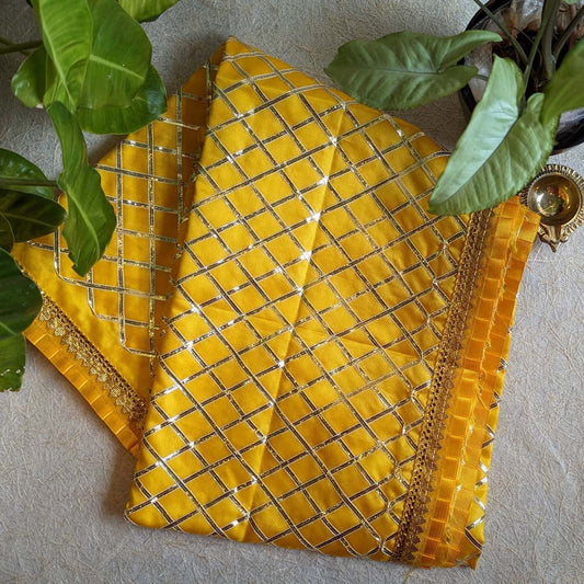 A 1-meter gold Chunari with a silver checkered pattern and a decorative border, displayed alongside green leaves and a brass diya.