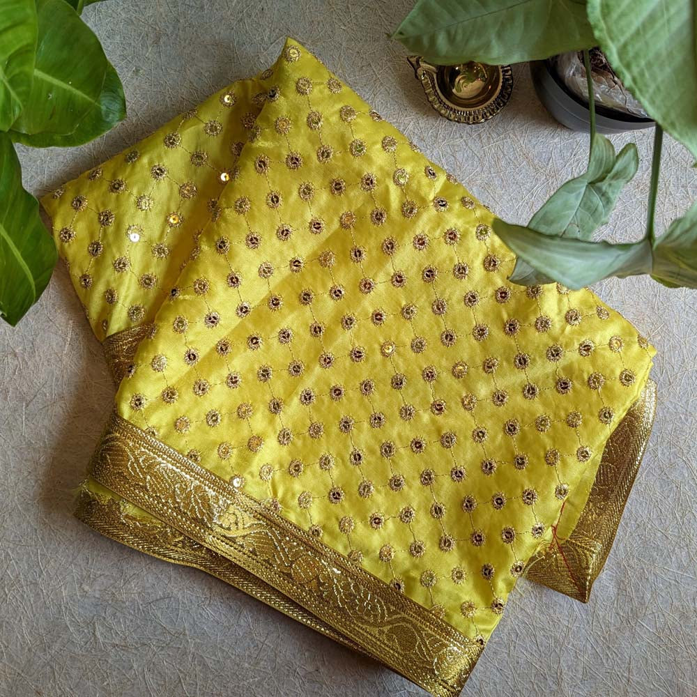 A 1-meter yellow Chunari adorned with intricate gold butis and a decorative golden border, displayed alongside green leaves and a brass diya.