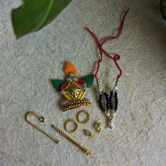 Handcrafted Krishna ornament set with a crown, beaded necklace, golden flute, earrings, anklets, and rings for deity decoration.