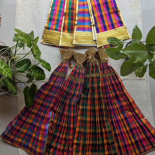 A vibrant multicolored checked Devi skirt with golden zari borders displayed alongside green indoor plants.