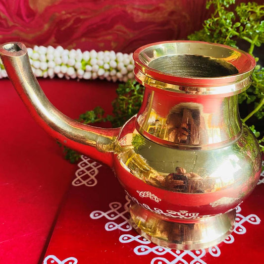 Handcrafted brass kindi with a polished finish, set on a red background adorned with intricate kolam designs.