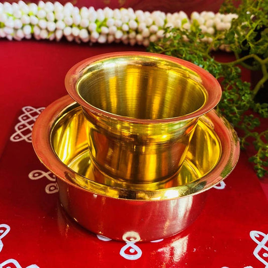 Handcrafted traditional brass dabra set with a tumbler and bowl, placed on a vibrant red background with kolam designs.