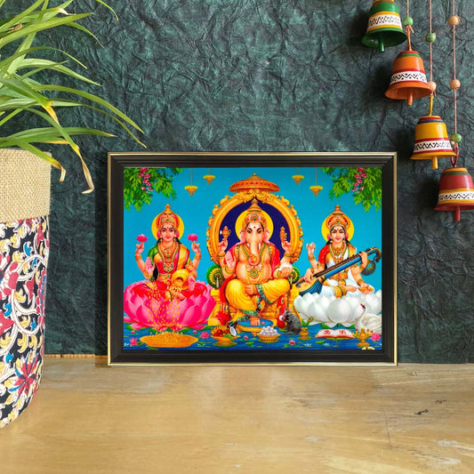 Framed artwork featuring Goddess Lakshmi, Lord Ganesha, and Goddess Saraswati with vibrant background and intricate detailing.