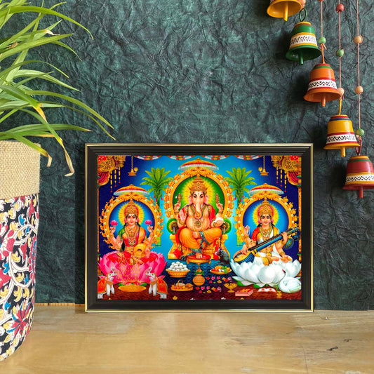 Lakshmi, Ganesha, and Saraswati framed artwork featuring the divine trio seated on lotus thrones with ornate arches and vibrant backdrops.